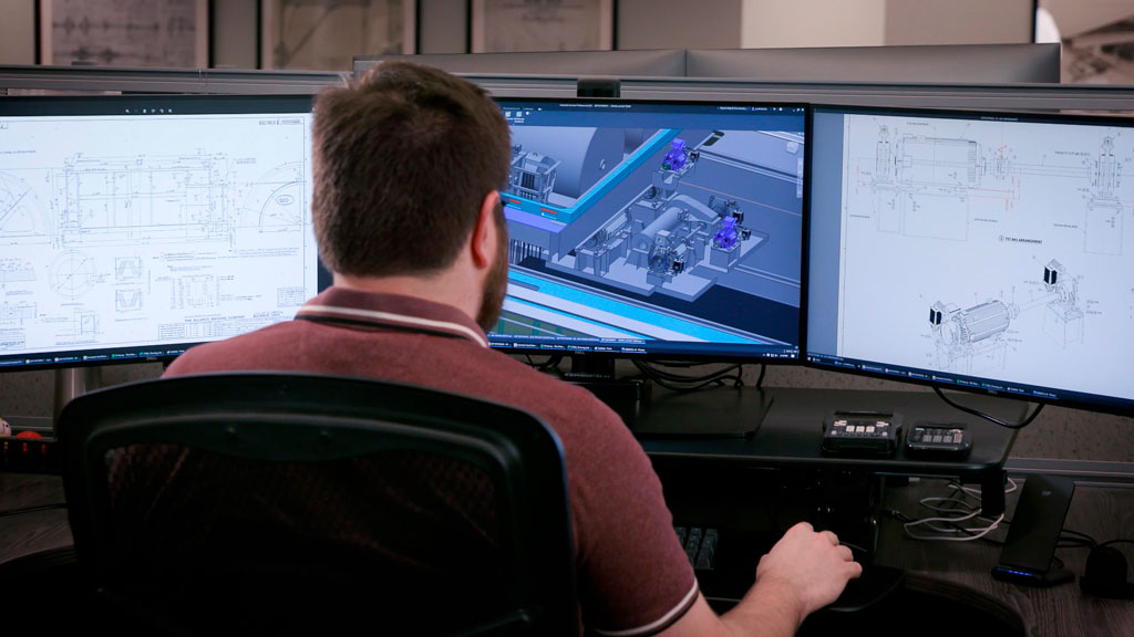 A Morgan male engineer using 3D imaging software on three desktop computers in an office.