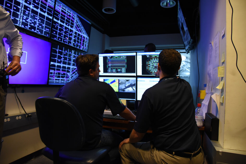 Two men reviewing a wall of computer screens