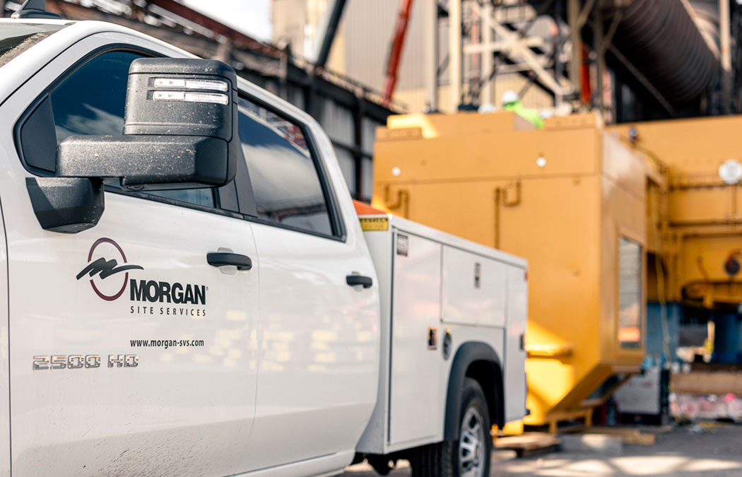 White Morgan Engineering pickup truck parked in front of a yellow Morgan Engineering crane outside of the warehouse.