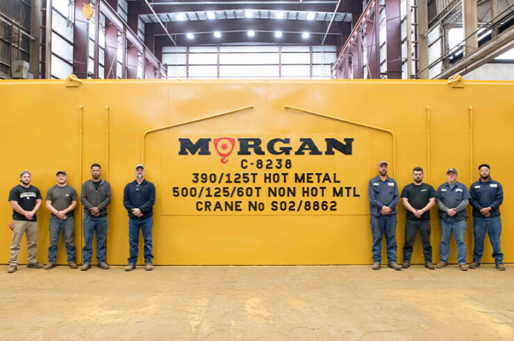 Eight men standing in front of a newly assembled yellow Morgan Crane in the Morgan warehouse.